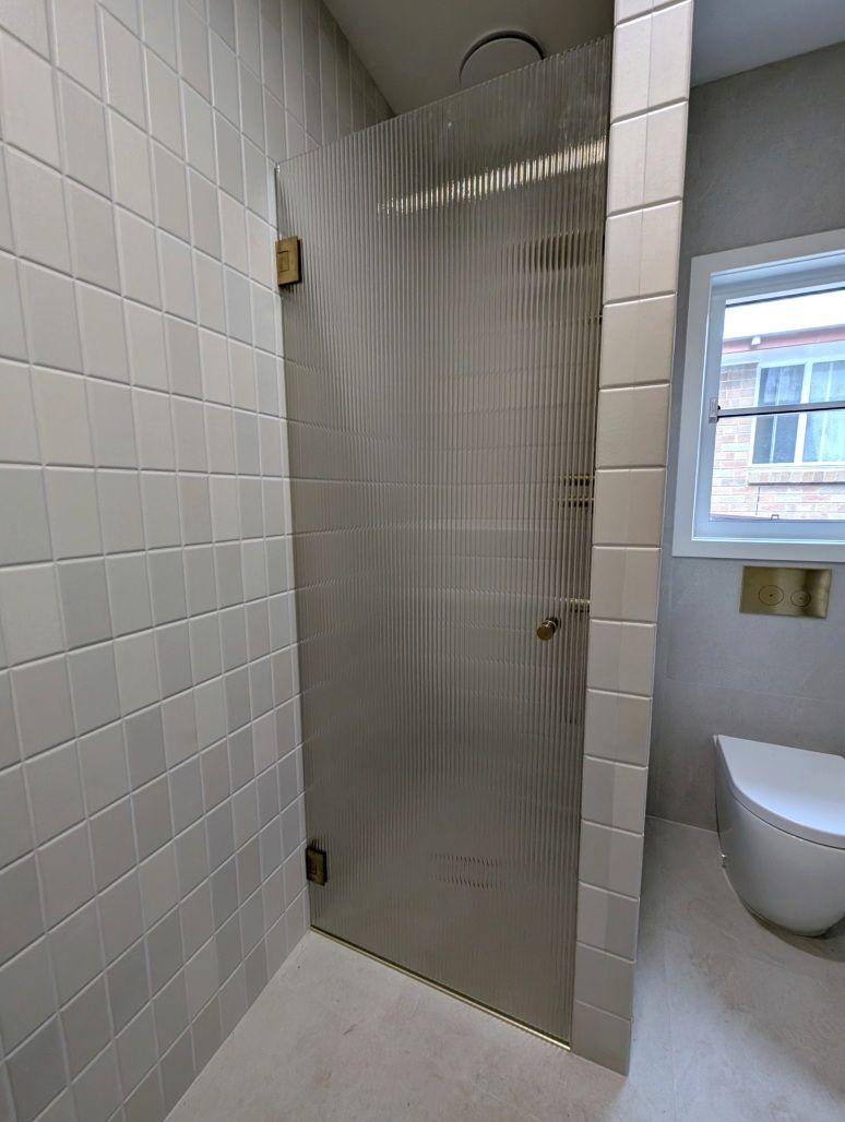 Fluted glass frameless shower door with brushed gold hinges