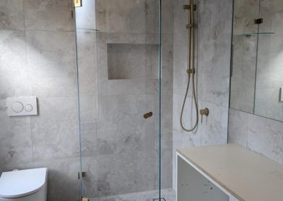 Frameless diamond shower screen with brushed brass hardware and built-in niche