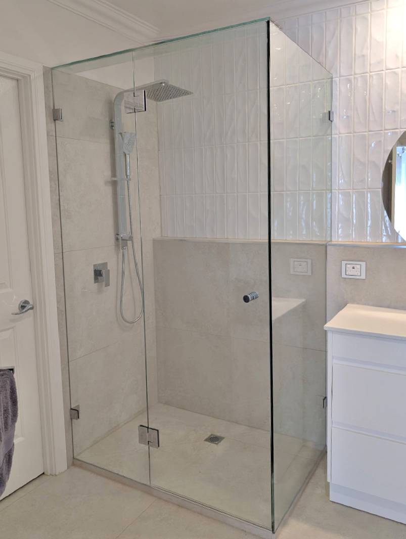 Frameless shower screen with chrome hardware in a light bathroom