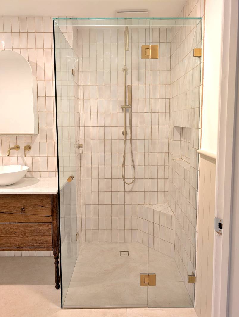 Cream coloured small format tiles and a frameless shower screen with brushed gold hardware
