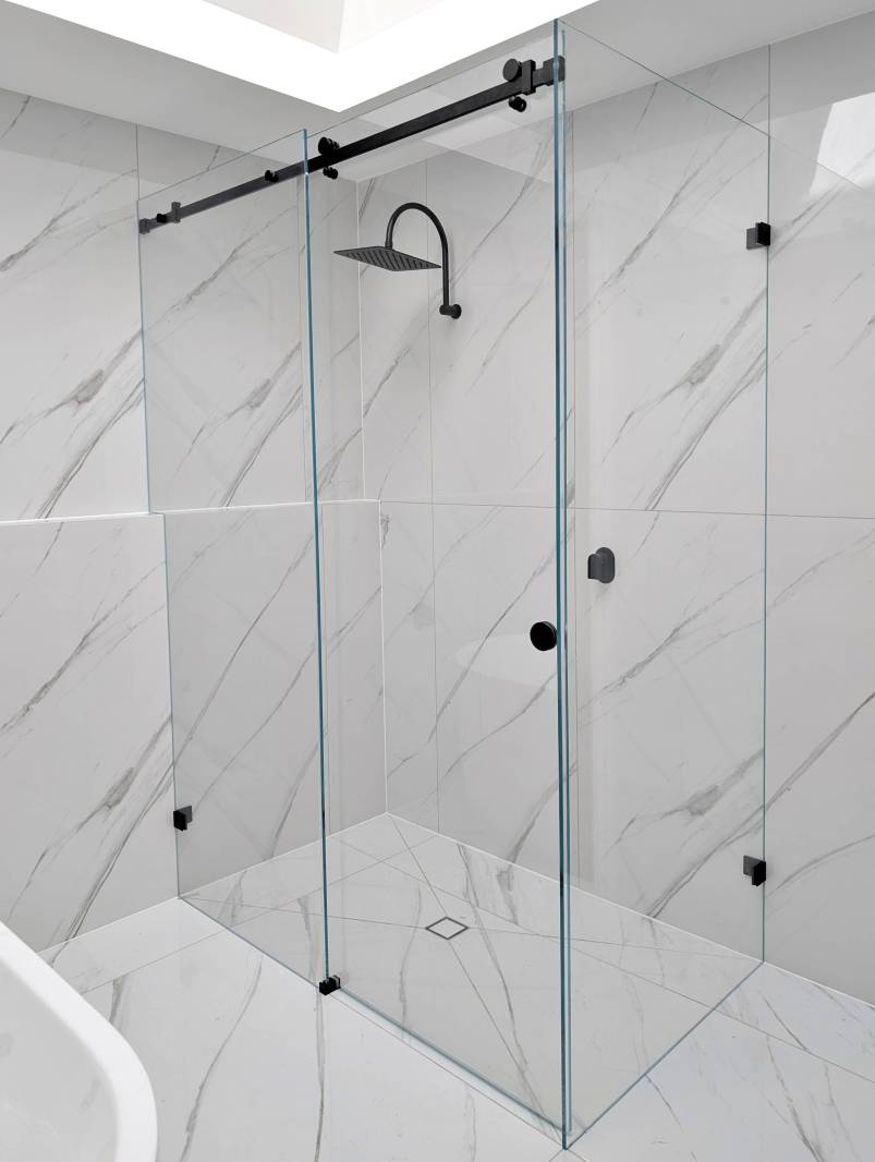 Frameless sliding shower screen with black fittings and marble look tiles